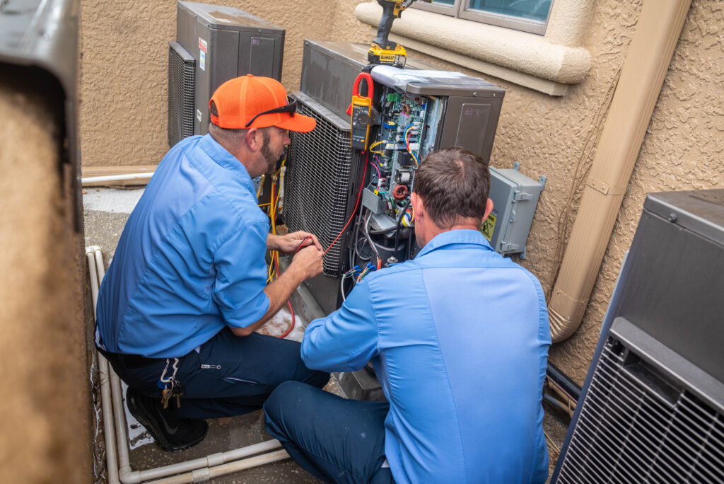 Two Sunshine State technicians in branded uniforms repairing an outdoor air conditioning condenser unit