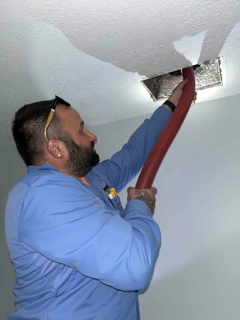 A Sunshine State technician inspecting a ceiling air duct vent during a service call